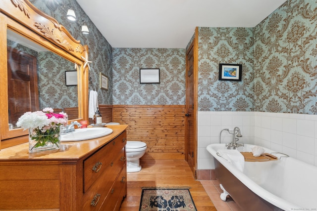 full bath with toilet, wallpapered walls, a freestanding tub, and a wainscoted wall