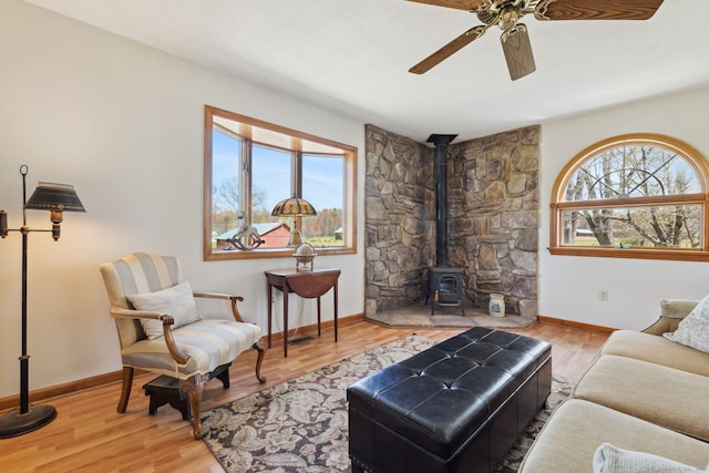 living area with ceiling fan, baseboards, a wood stove, and wood finished floors