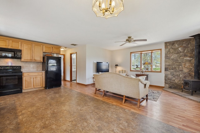 living area with ceiling fan with notable chandelier, baseboards, a wood stove, and light wood finished floors