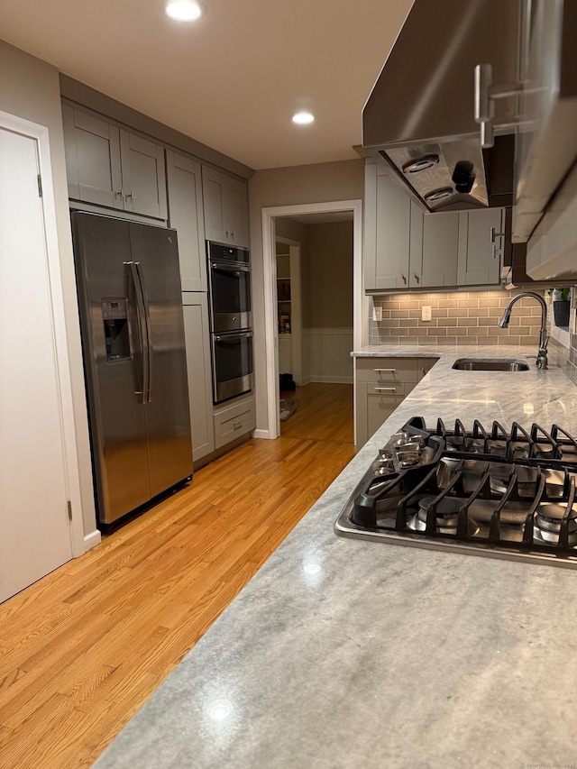 kitchen featuring a sink, range hood, gray cabinetry, and stainless steel appliances