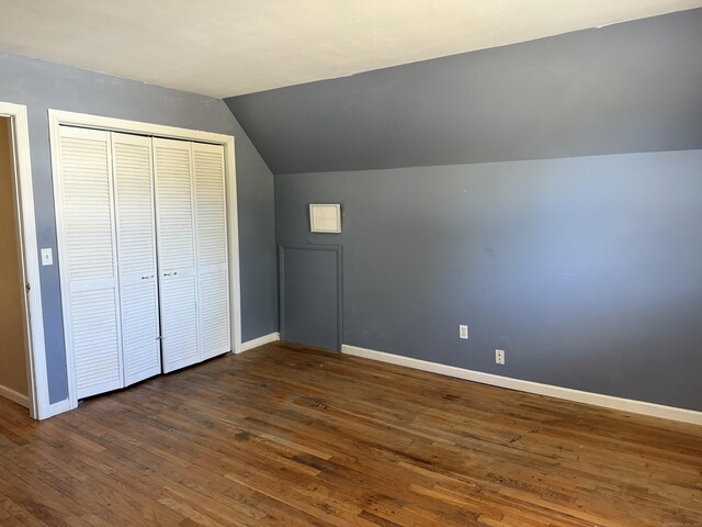 unfurnished bedroom featuring baseboards, lofted ceiling, a closet, and dark wood-type flooring