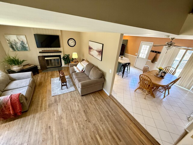 living room with baseboards, light wood-type flooring, ceiling fan, and a glass covered fireplace
