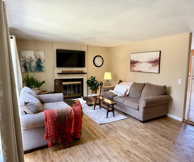 living room with baseboards, a glass covered fireplace, and light wood-type flooring