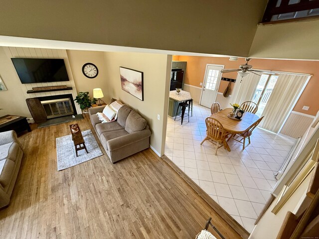living room featuring light wood-type flooring, a high ceiling, a glass covered fireplace, and a ceiling fan
