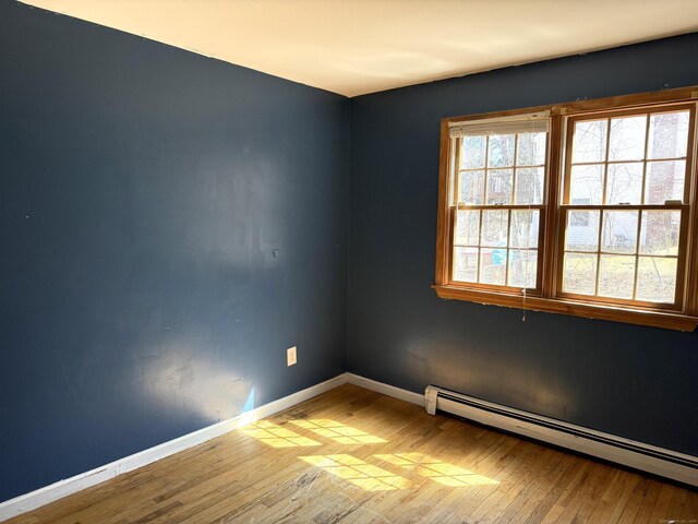 empty room with baseboards, a baseboard heating unit, and wood-type flooring