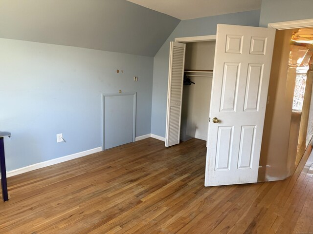 unfurnished bedroom with wood-type flooring, a closet, baseboards, and lofted ceiling