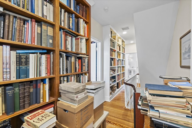 interior space featuring bookshelves, wood finished floors, visible vents, and recessed lighting