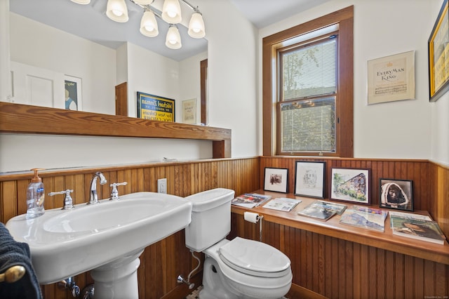 bathroom with wainscoting, wooden walls, a sink, and toilet