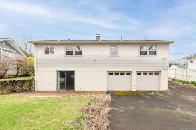 rear view of property with stucco siding, an attached garage, fence, driveway, and a lawn