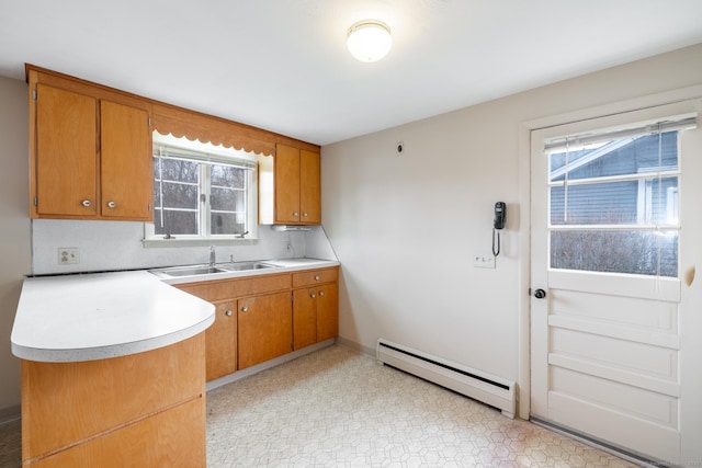 kitchen with a sink, light countertops, baseboard heating, a wealth of natural light, and brown cabinetry