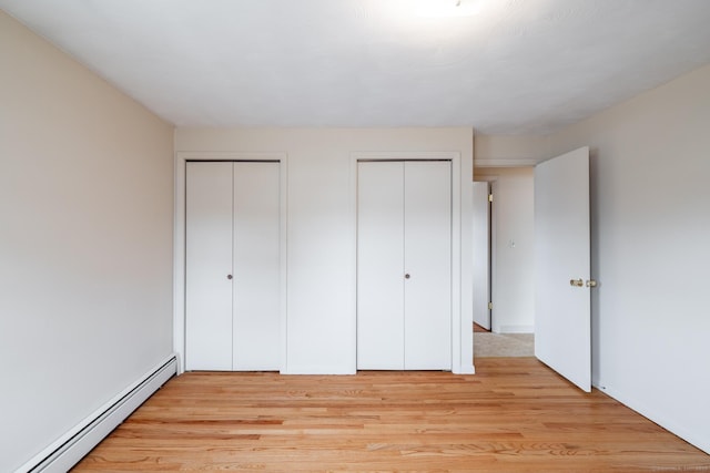 unfurnished bedroom with light wood-style flooring, two closets, and a baseboard radiator