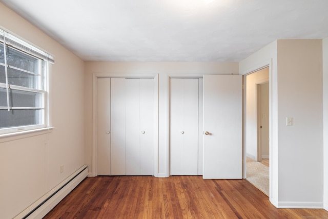 unfurnished bedroom with two closets, baseboards, wood finished floors, and a baseboard radiator