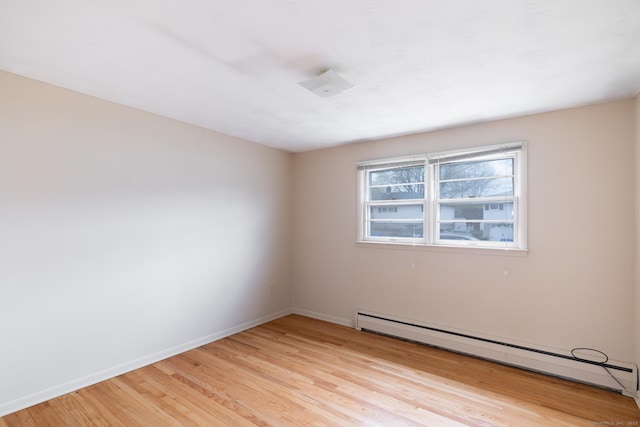 spare room featuring a baseboard heating unit, light wood-style flooring, and baseboards