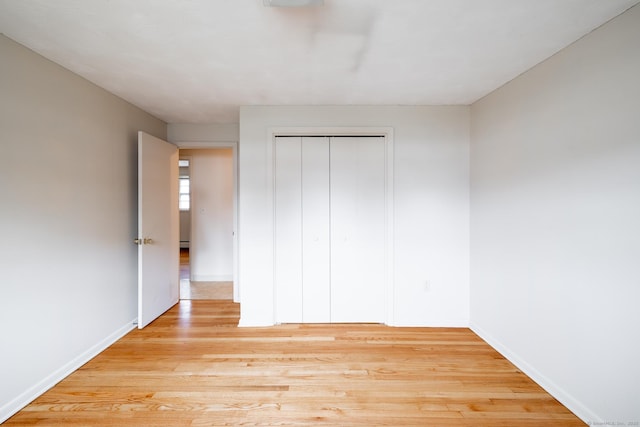 unfurnished bedroom with a closet, baseboards, a baseboard radiator, and light wood-style floors