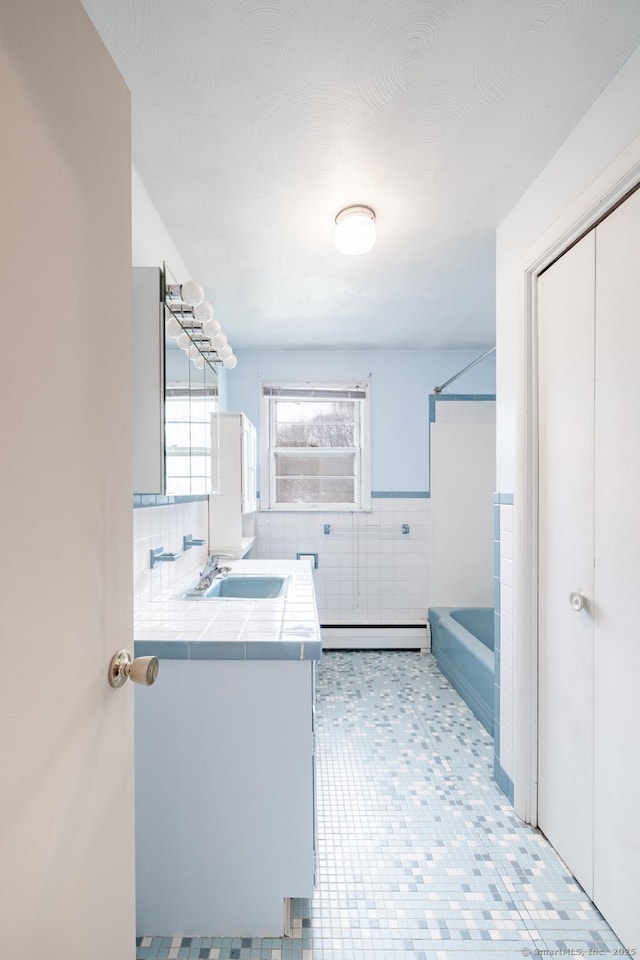 bathroom with tile walls, bathing tub / shower combination, a baseboard heating unit, and vanity