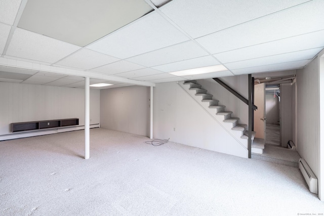 finished below grade area with a drop ceiling, carpet flooring, a baseboard heating unit, and stairs