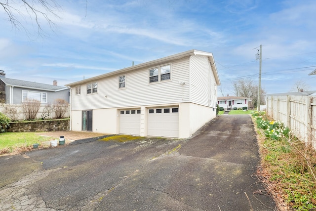 exterior space featuring a garage, fence, stucco siding, and driveway