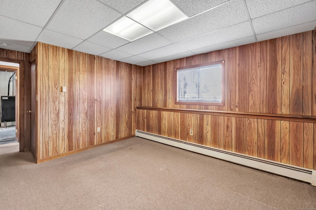 carpeted empty room featuring baseboard heating, wood walls, and a drop ceiling