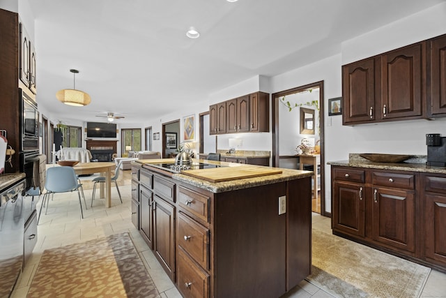 kitchen with ceiling fan, a fireplace, built in microwave, open floor plan, and a center island with sink