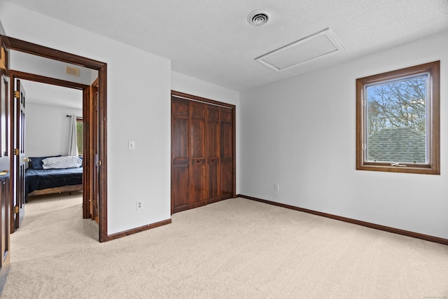 unfurnished bedroom featuring light colored carpet, attic access, baseboards, and visible vents