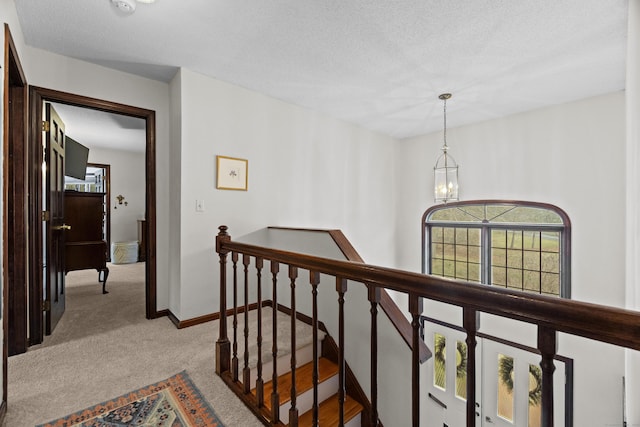 hall with baseboards, a textured ceiling, a chandelier, carpet flooring, and an upstairs landing