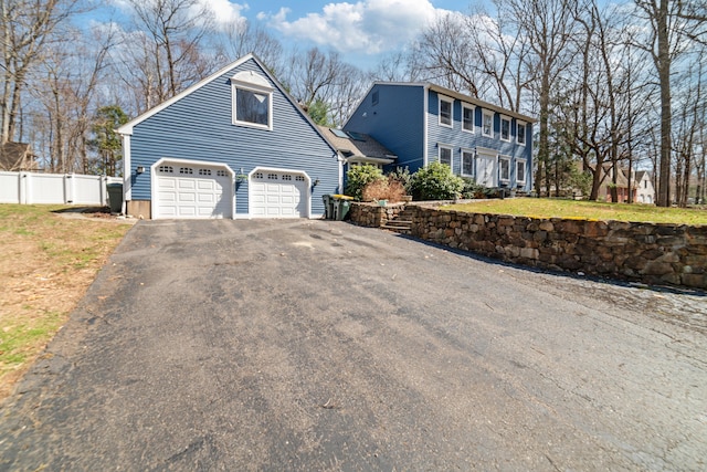 colonial home featuring driveway, a garage, fence, and a front lawn