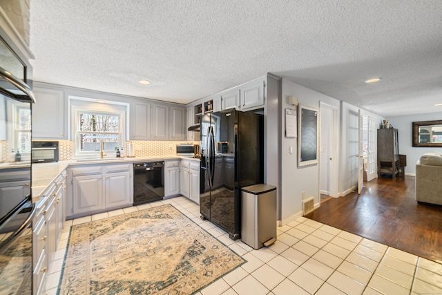 kitchen featuring light tile patterned flooring, light countertops, a sink, tasteful backsplash, and black appliances