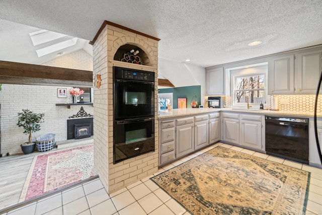 kitchen featuring a wood stove, gray cabinets, light tile patterned floors, vaulted ceiling with skylight, and black appliances