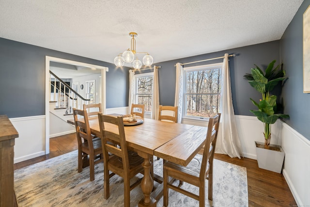 dining space with a wainscoted wall, stairs, wood finished floors, and an inviting chandelier