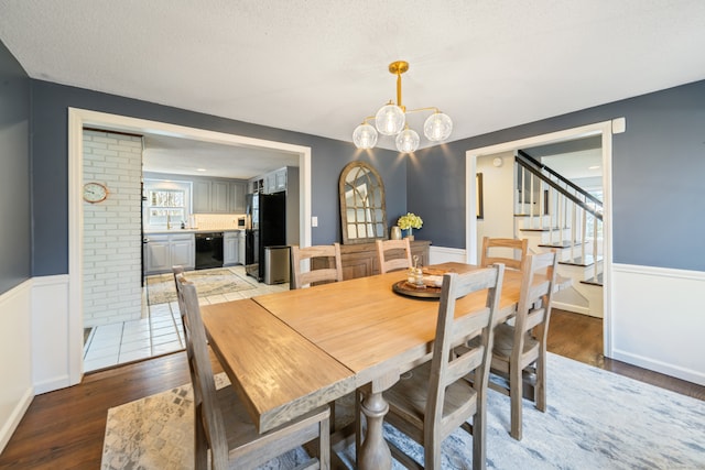 dining space featuring wood finished floors, stairway, an inviting chandelier, a textured ceiling, and wainscoting
