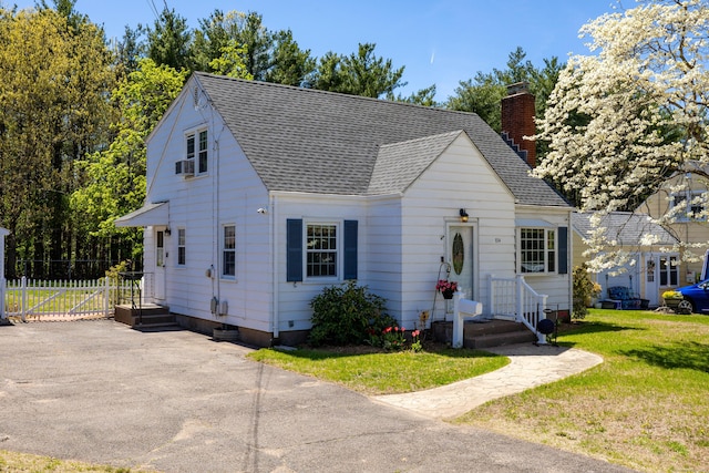 view of front facade featuring a chimney, roof with shingles, and a front lawn