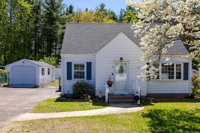 view of front facade featuring roof with shingles, a front lawn, a detached garage, an outbuilding, and driveway