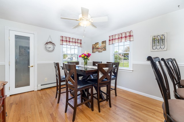 dining room featuring a ceiling fan, a wealth of natural light, baseboard heating, and light wood finished floors