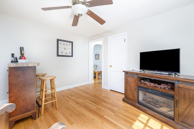 living area with baseboards, ceiling fan, and light wood-style floors