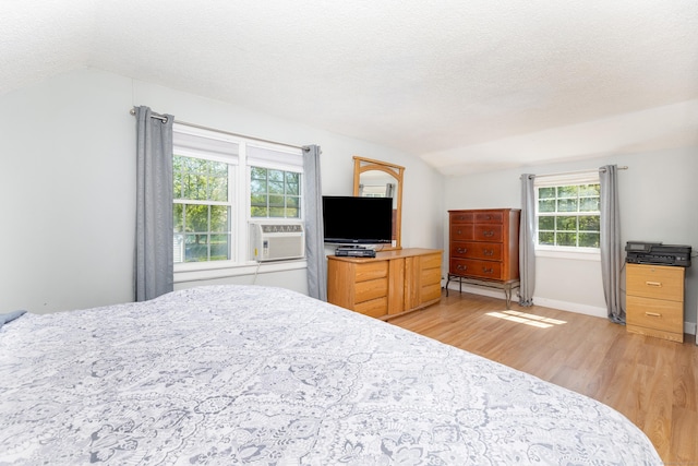 bedroom featuring a textured ceiling, cooling unit, vaulted ceiling, and light wood-style flooring