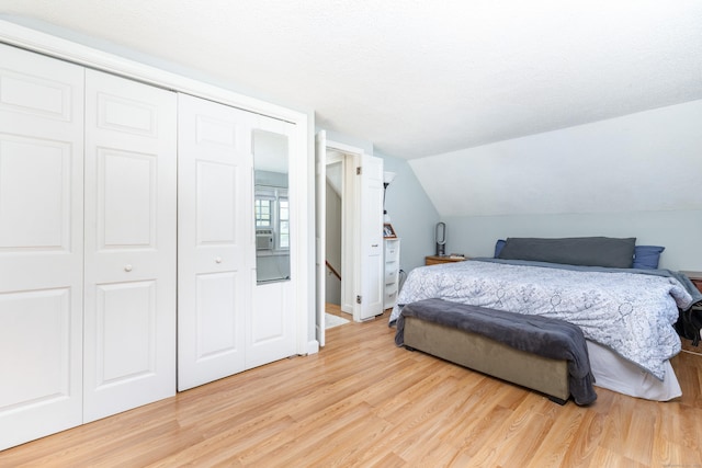 bedroom with light wood-style floors, vaulted ceiling, and a closet