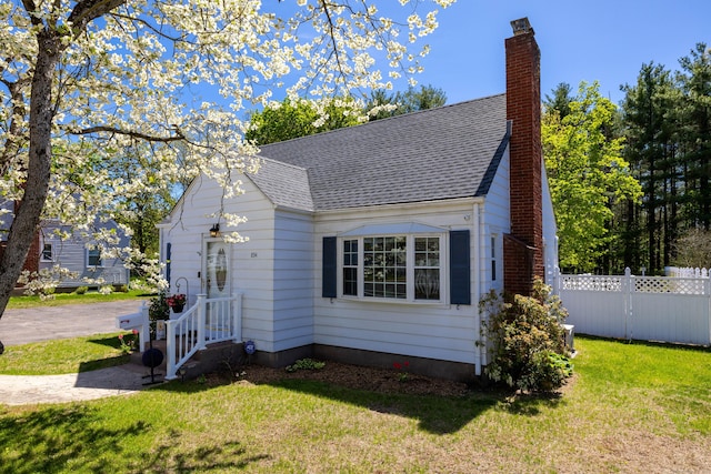 view of side of home featuring fence, a chimney, a lawn, and roof with shingles