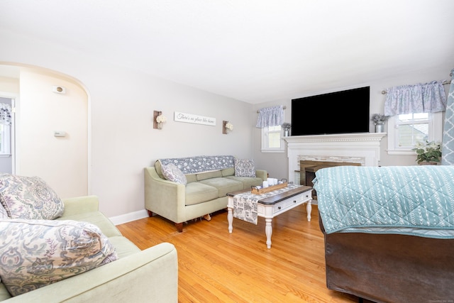 living room featuring a high end fireplace, arched walkways, light wood-style flooring, and baseboards