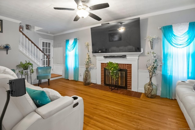 living room featuring wood finished floors, stairway, ceiling fan, crown molding, and a fireplace