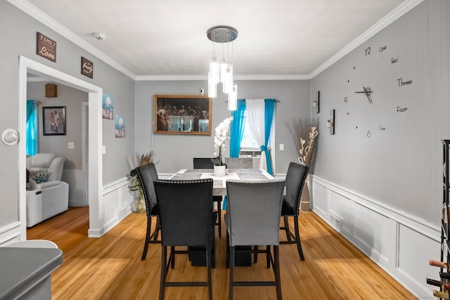 dining space with ornamental molding, light wood-style floors, a wainscoted wall, a decorative wall, and a chandelier