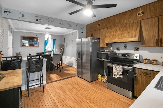kitchen with stainless steel appliances, a ceiling fan, light wood-style floors, wainscoting, and ornamental molding