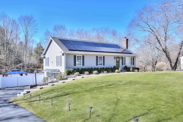 ranch-style home featuring a chimney, solar panels, and a front lawn