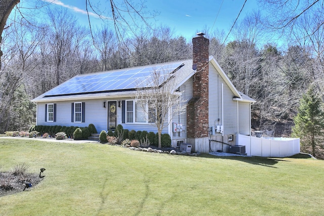 ranch-style home with a chimney, solar panels, and a front yard