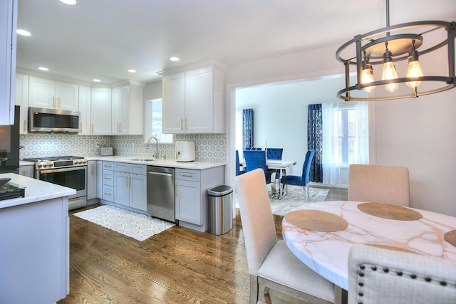 kitchen with a sink, a chandelier, stainless steel appliances, dark wood-type flooring, and backsplash