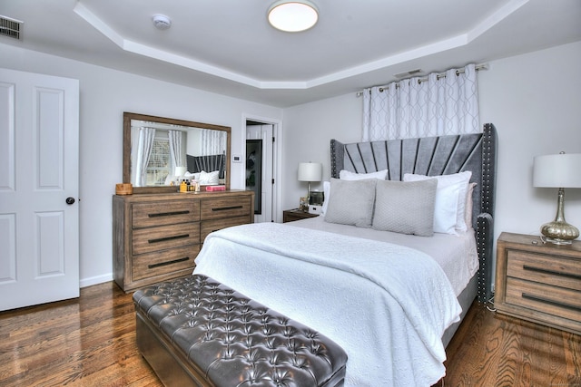 bedroom with a tray ceiling, visible vents, and dark wood-type flooring