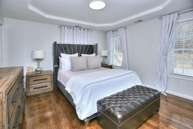 bedroom with a raised ceiling, baseboards, wood finished floors, and visible vents