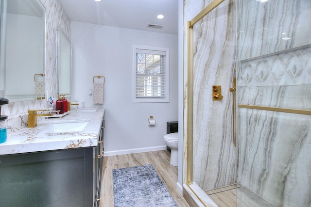 full bathroom with vanity, toilet, a marble finish shower, wood finished floors, and visible vents