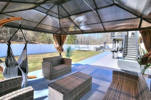 view of patio with an outdoor living space, a trampoline, a gazebo, a fenced backyard, and stairs