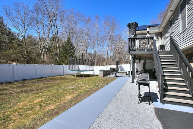 view of yard featuring a trampoline, a deck, a patio area, stairway, and a fenced backyard