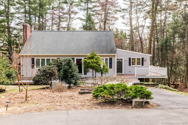 cape cod-style house with a chimney, a deck, and aphalt driveway